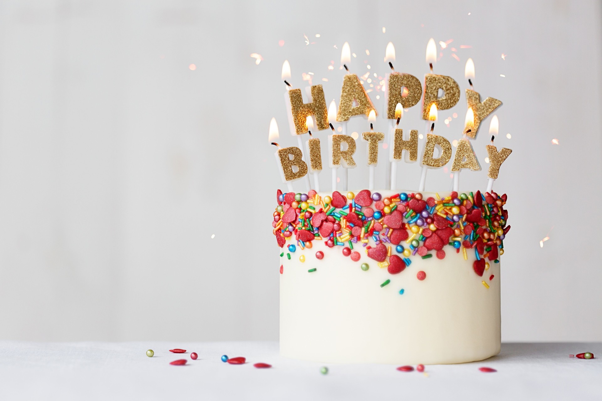 Happy birthday cake with gold candles and heart shaped sprinkles
